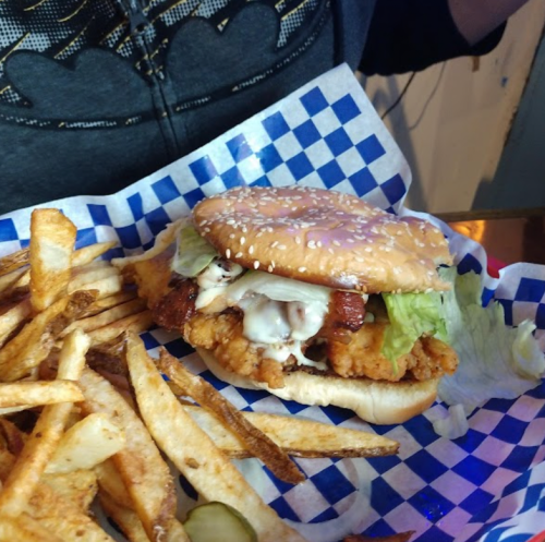 A sesame seed bun sandwich with fried chicken, lettuce, and sauce, served with a side of golden fries.