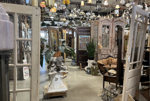 A spacious vintage shop filled with various doors, light fixtures, and decorative items, creating an eclectic atmosphere.