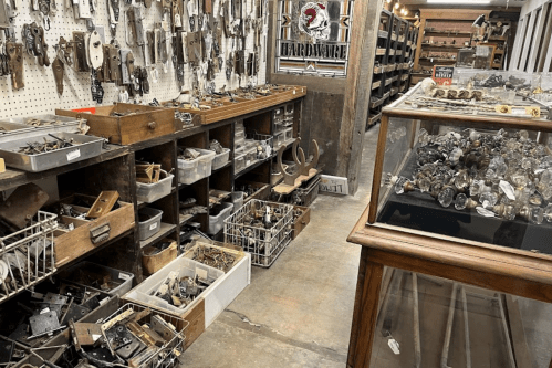 A vintage hardware store aisle filled with various tools, drawers, and containers of hardware items.