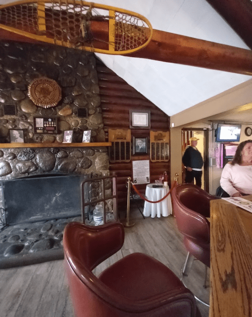 Cozy interior of a rustic lodge with a stone fireplace, wooden beams, and red leather chairs.