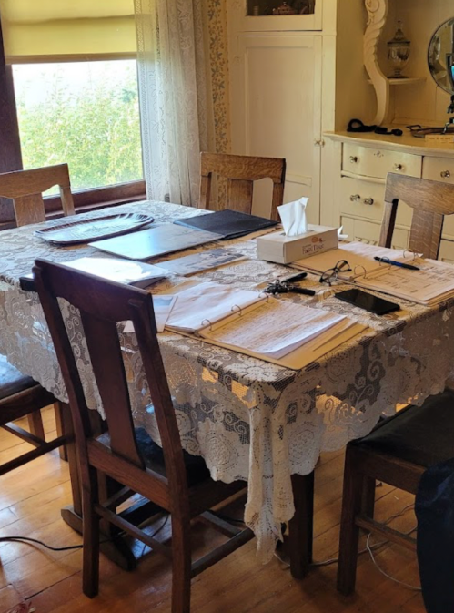 A dining table set with papers, a tissue box, and chairs, surrounded by a cozy, well-lit room.