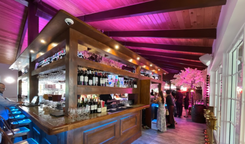 A stylish bar with wooden accents, colorful lighting, and patrons enjoying drinks in a lively atmosphere.