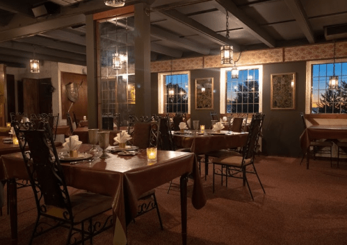 Cozy restaurant interior with tables set for dining, warm lighting, and large windows showcasing a sunset view.