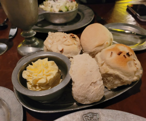 A silver platter with assorted bread rolls and a small bowl of butter.