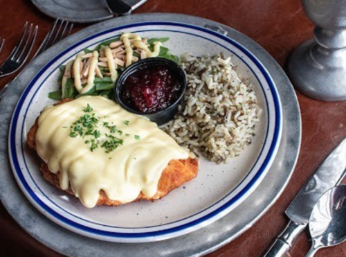 A plate featuring breaded chicken topped with cheese, served with rice, green salad, and a side of cranberry sauce.