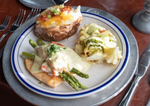 A plate with a baked potato, creamy fish topped with asparagus, and a side of mixed vegetables.