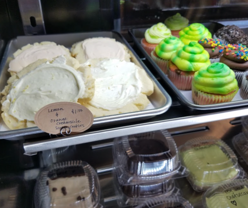 A display case with lemon and orange cookies, and colorful cupcakes with green frosting and sprinkles.