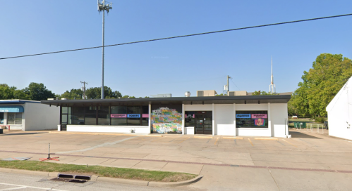 A storefront with large windows and colorful signage, set against a clear blue sky. Nearby utility poles are visible.