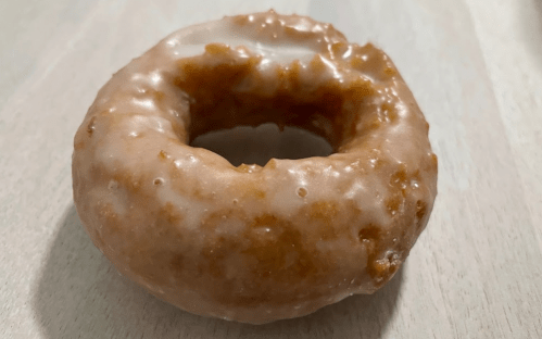 A glazed donut with a light brown color, resting on a wooden surface.