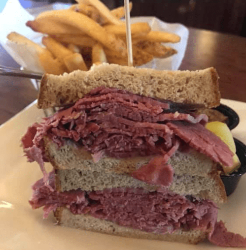 A stacked sandwich with layers of corned beef on rye bread, served with a side of fries.