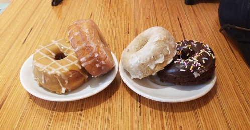 Three donuts on two plates: one glazed, one chocolate with sprinkles, and one with a light frosting.