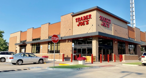 Exterior of a Trader Joe's store with a stop sign and parked cars in the foreground. Bright, sunny day.