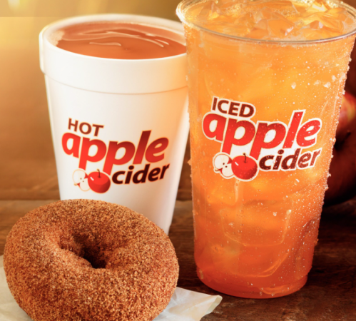 A cup of hot apple cider, a cup of iced apple cider, and a cinnamon sugar donut on a wooden surface.