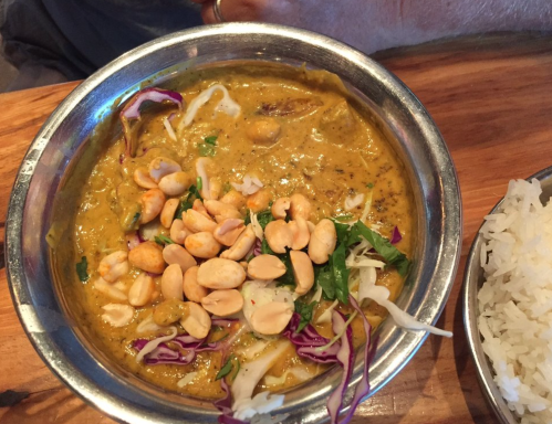A bowl of curry topped with peanuts and fresh herbs, served alongside a portion of white rice.