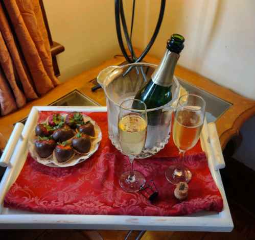 A tray with champagne, two glasses, and chocolate-covered strawberries on a red cloth.
