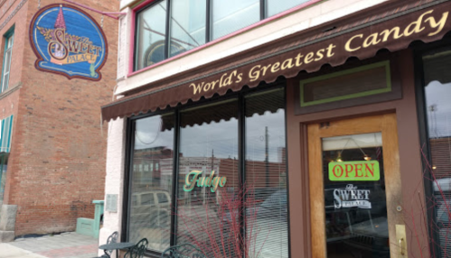 Exterior of The Sweet Palace candy shop, featuring a sign that reads "World's Greatest Candy" and an "Open" notice.