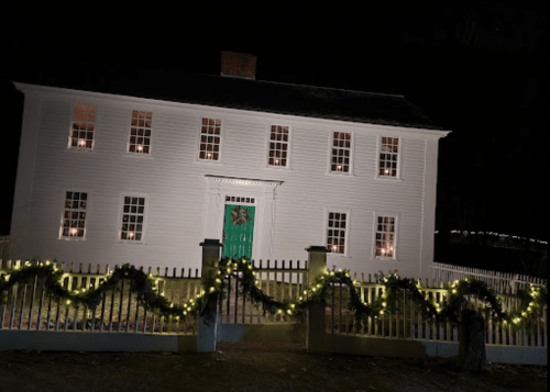 A white house with green door, decorated with lights and garlands, set against a dark night sky.