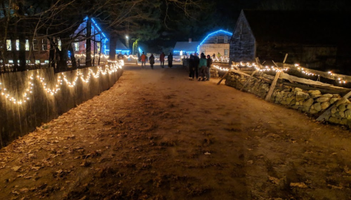 A dimly lit path lined with festive lights, leading to buildings, with people walking in the distance on a fall evening.
