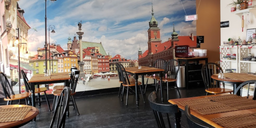 Cozy café interior with wooden tables, black chairs, and a mural of a cityscape featuring historic buildings.