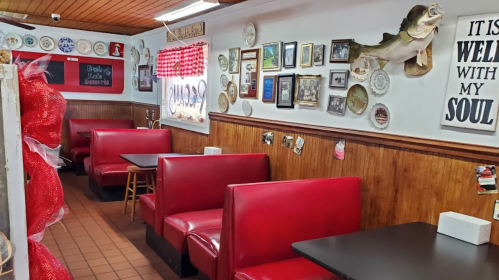 Cozy restaurant interior with red booths, wooden walls, and various framed pictures and plates on display.
