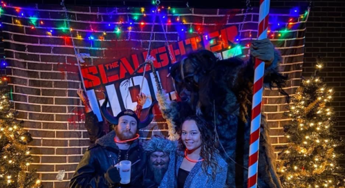 A festive scene with three people posing in front of a decorated backdrop, featuring holiday lights and a large sign.