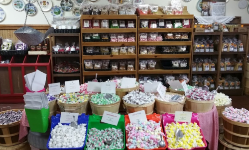 A colorful display of various candies in baskets, with shelves of packaged treats in the background.