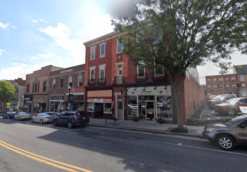 A street view of a small town with brick buildings, shops, and parked cars under a clear blue sky.