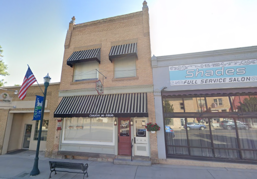 A brick building with striped awnings, featuring a sign for "Candies on Main" and a nearby salon, with an American flag.