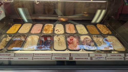 A display case filled with various ice cream flavors in metal tubs, including chocolate chip, mint chip, and vanilla bean.