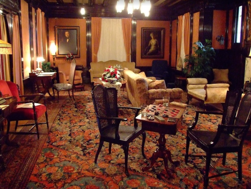 A cozy, vintage living room with ornate furniture, a patterned rug, and soft lighting, featuring a checkers table.