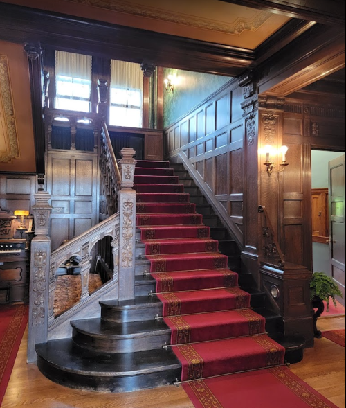 Elegant wooden staircase with red carpet, ornate railings, and rich wall paneling in a grand entryway.