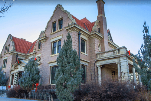 Historic mansion with decorative greenery and red bows, featuring a distinctive architectural style and a landscaped yard.