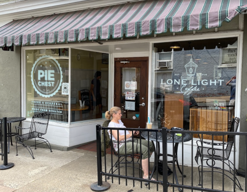 A woman sits at a table outside a café with a sign reading "Lone Light Coffee" and "Pie Chest."