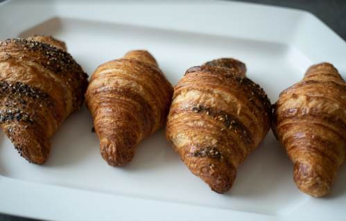 Four golden-brown croissants with a flaky texture, arranged neatly on a white platter.