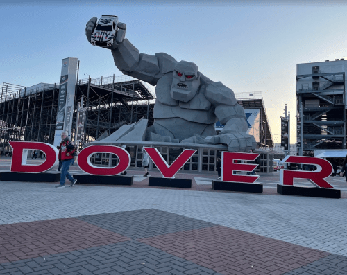 A large stone statue of a monster holding a racing car, with the word "DOVER" in bold letters in the foreground.