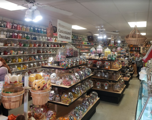 A colorful candy store filled with jars of sweets, chocolates, and treats on shelves, with customers browsing.