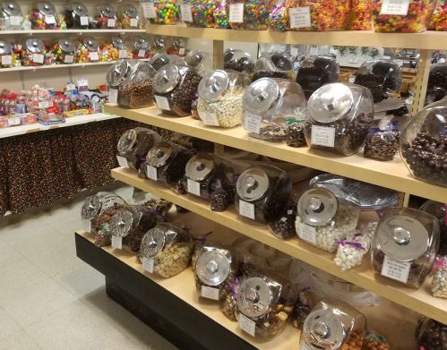 A colorful candy store display with jars of various candies on shelves and a table covered in candy.