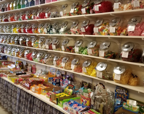A colorful candy shop display with jars of various candies on shelves and assorted sweets on the counter below.