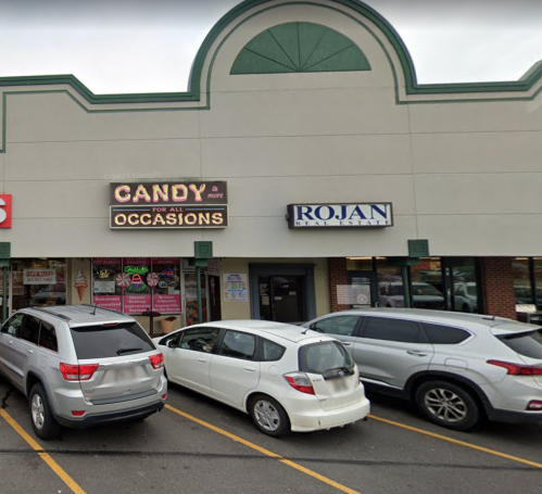 A storefront with a candy shop sign and a real estate office, featuring parked cars in front.