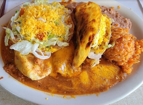 A plate of enchiladas topped with cheese, lettuce, and tomatoes, served with rice and refried beans.