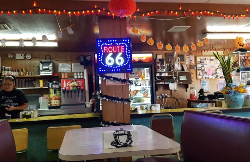 A cozy diner interior with a "Route 66" neon sign, festive decorations, and a table with a coffee cup drawing.