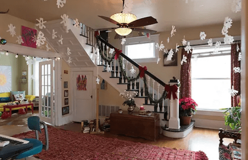 Cozy living room decorated for the holidays, featuring a staircase, festive decor, and a warm atmosphere.