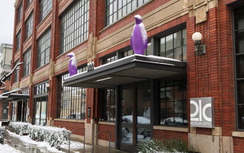 Entrance of a hotel with large purple penguin sculptures on the roof, surrounded by snow-covered ground and buildings.