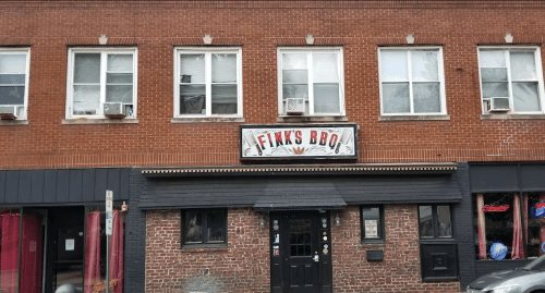 Exterior of Fink's BBQ restaurant, featuring a brick facade and large sign above the entrance. Windows with air conditioners visible.