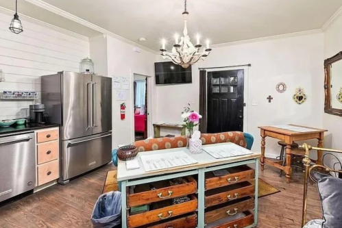 A cozy kitchen with a chandelier, stainless steel appliances, a wooden table, and a decorative island with drawers.