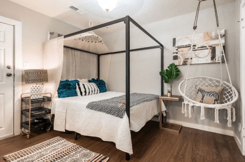 Cozy bedroom with a four-poster bed, hanging chair, and decorative plants, featuring warm wood flooring and soft textiles.