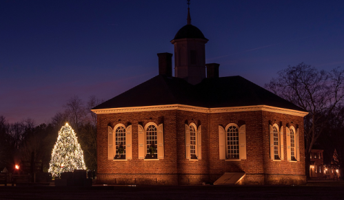 Historic brick building illuminated at dusk, with a large, decorated Christmas tree nearby.