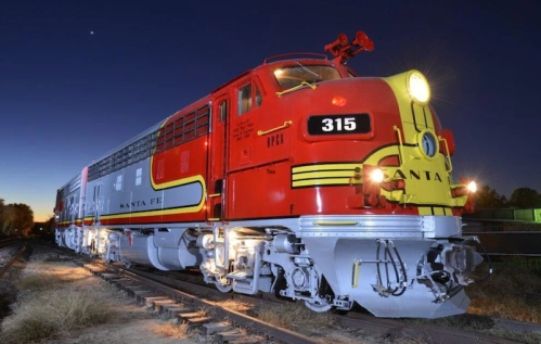 A vintage red and yellow Santa Fe locomotive at dusk, illuminated against a darkening sky.