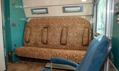 Interior of a vintage trailer featuring a patterned couch and a blue chair against a turquoise wall.