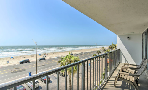 View from a balcony overlooking a beach with palm trees and waves under a clear blue sky.
